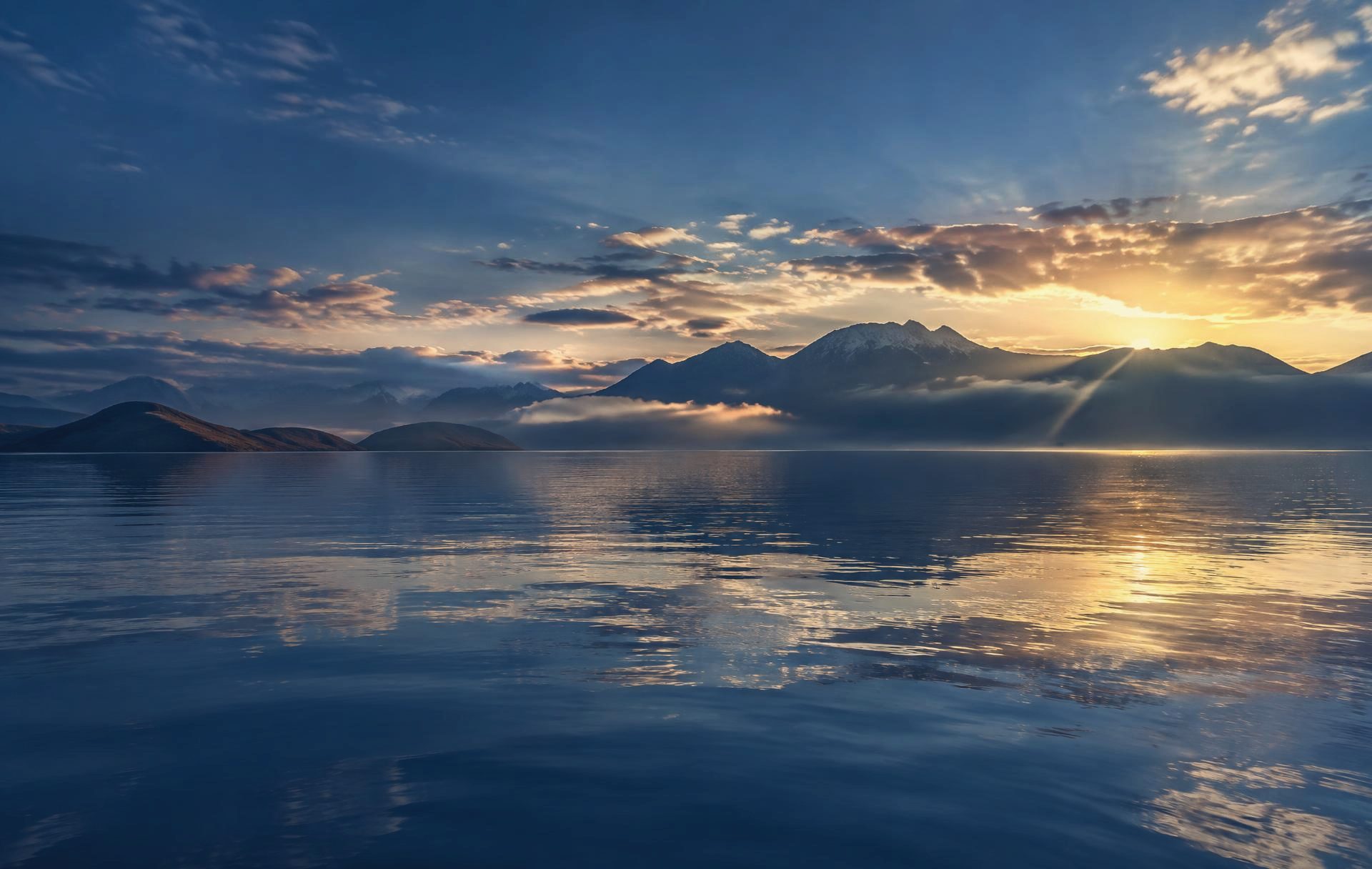 Amanhecer sobre as águas calmas do Lago Titicaca, com montanhas ao fundo